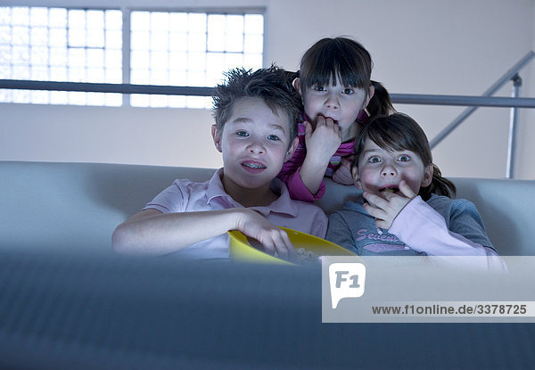 Kinder sitzen mit einer Schüssel Popcorn vor dem Fernseher  Frontalansicht
