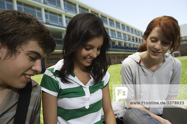 Teenager-Freunde  die draußen auf dem Schulrasen sitzen.