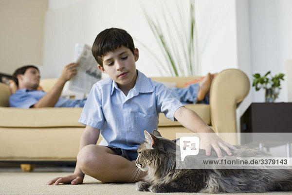 Kleiner Junge sitzt im Wohnzimmer und streichelt Katze