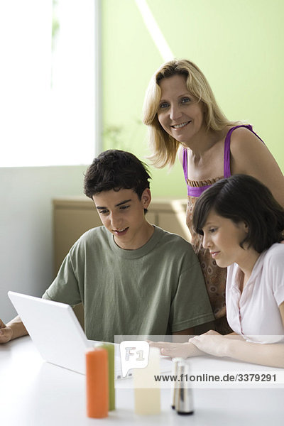 Mother observing teenage son and daughter using laptop computer