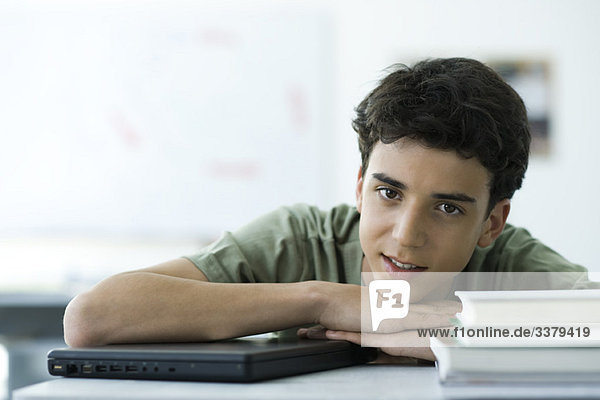 Gymnasiast am Schreibtisch sitzend mit auf den Armen liegendem Kopf  Portrait