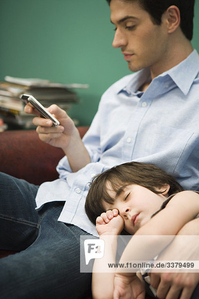 Junger Mann SMS  während der Sohn mit dem Kopf im Schoß schläft.