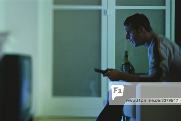 Mann beim Fernsehen  hält Bier und Fernbedienung  Seitenansicht