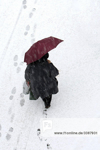Frau mit Regenschirm und Einkaufstüten läuft durch den Schnee  Vogelperspektive