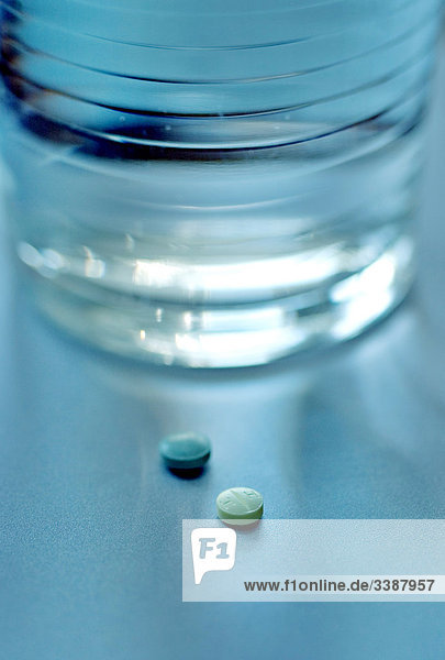 Zwei Tabletten liegen neben Wasserglas  Close-up