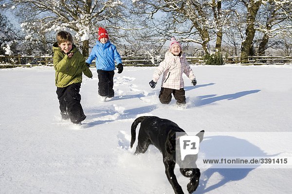 Kinder und Hund rennen im Schnee