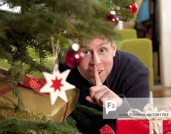 Mann versteckt Geschenke unter dem Weihnachtsbaum