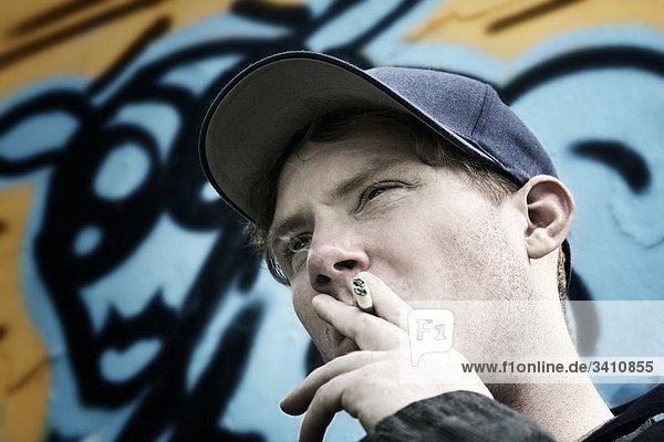 Junger Mann mit Zigarette und Kappe vor Graffitiwand