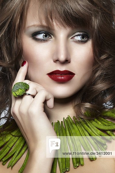 Junge Frau mit einer Kette aus grünen Bohnen und einem Ring aus Broccoli mund