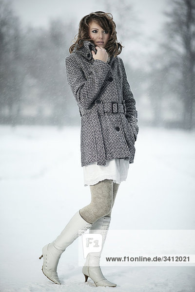 Junge Frau steht mit Poncho im Schnee
