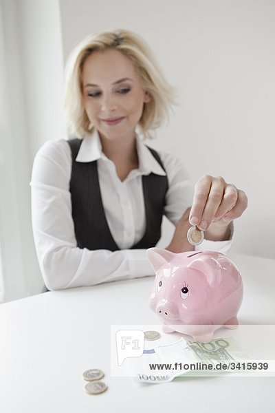 Frau lässt Geld ins Sparschwein fallen