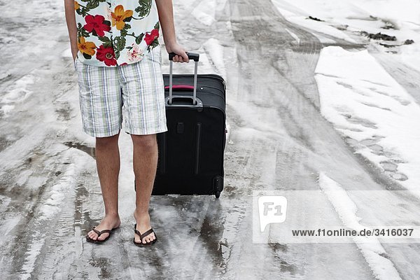 Mann in Sommerkleidung mit Koffer im Schnee