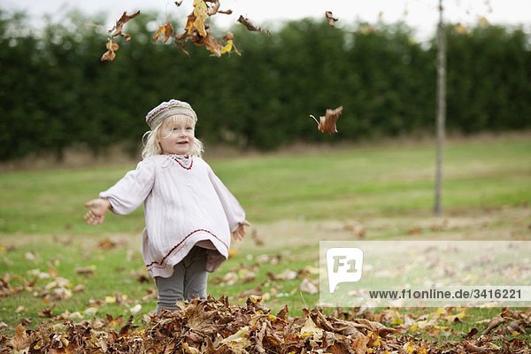Kleines Mädchen wirft Blätter in die Luft