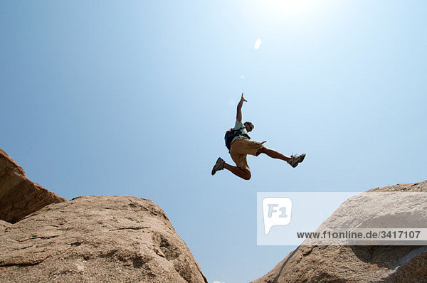 Mann springt zwischen großen Felsblöcken.