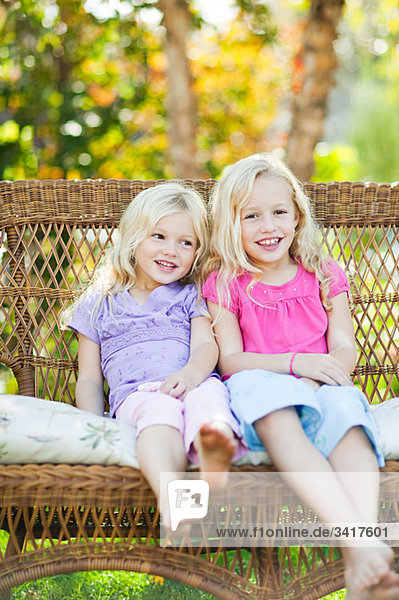 Sisters sitting on seat in garden