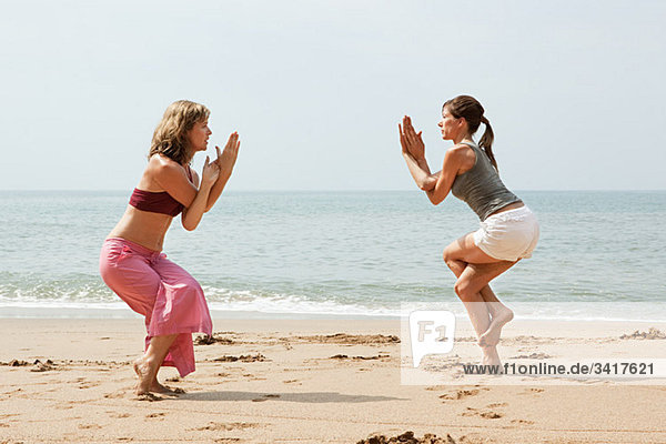 Two women practicing yoga on a beach
