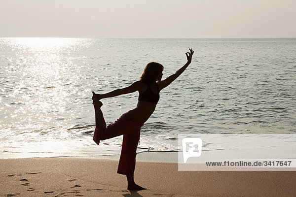 Frau praktiziert Yoga am Meer bei Sonnenuntergang