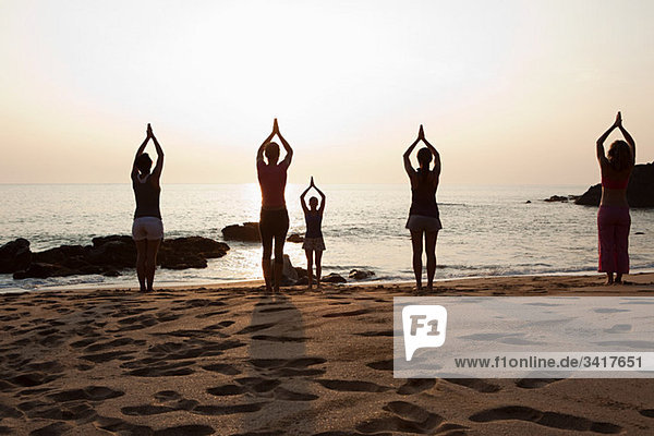 Frauen beim Yoga am Strand bei Sonnenuntergang