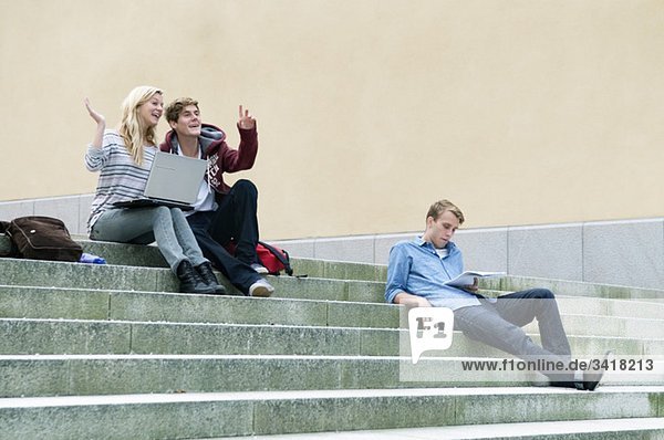 Drei glückliche Schüler auf einer Steintreppe mit Laptop