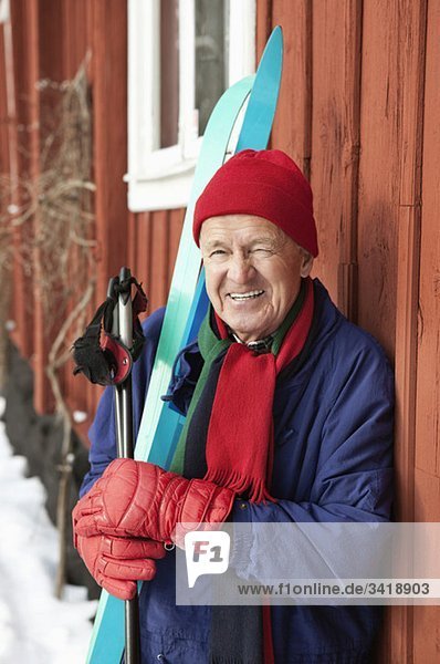 Nahaufnahme eines glücklichen Mannes  der draußen steht und Skier hält.