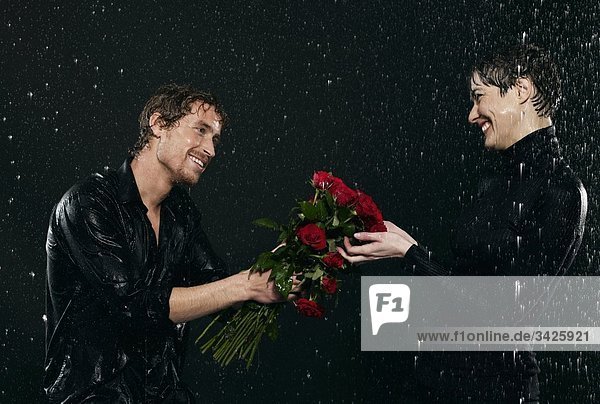 Männer bieten Blumenstrauß für Frauen bei Regen an.