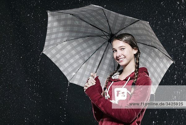 Mädchen steht im Regen  hält Regenschirm.