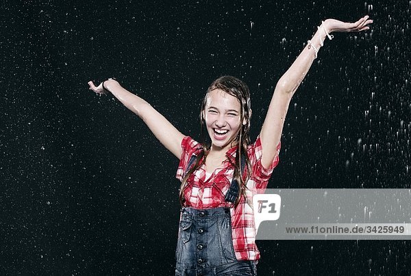 Mädchen im Regen stehend  Arme hoch  lächelnd.