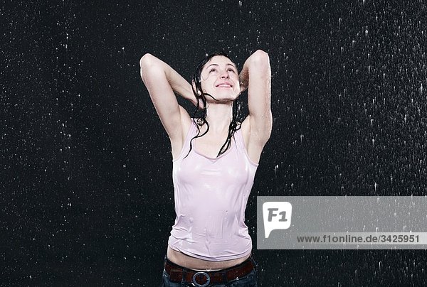 Frau im Regen stehend  Hände hinter dem Kopf  lächelnd.