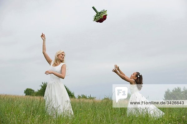 Braut und Blumenmädchen (4-5) beim Spielen mit Blumenstrauß auf der Wiese