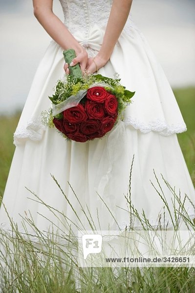 Bride standing on meadow holding bouquet  mid section  close-up