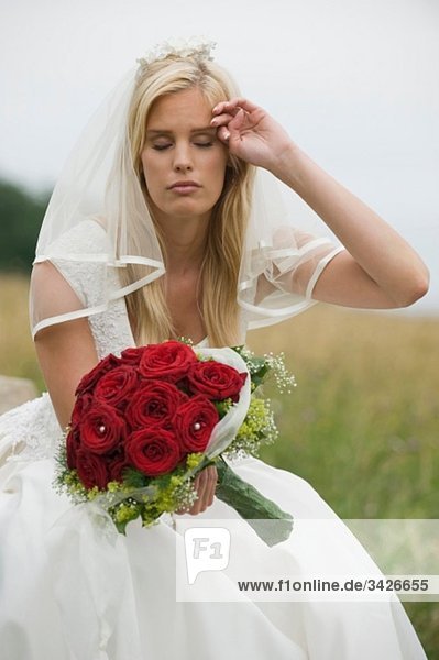 Braut sitzend mit Blumenstrauß  Kopf in Hand.