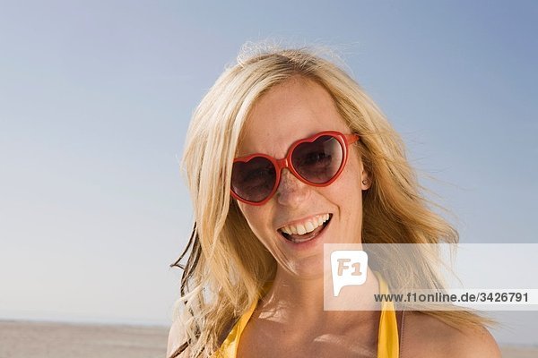 Deutschland  Schleswig Holstein  Amrum  Frau am Strand mit Sonnenbrille  Lachen  Portrait  Nahaufnahme