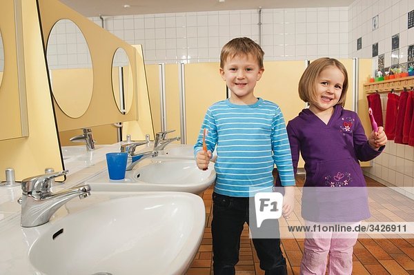 Deutschland  Junge (4-5) und Mädchen (3-4) stehen Hand in Hand in der Toilette mit Zahnbürsten  lächelnd  Portrait