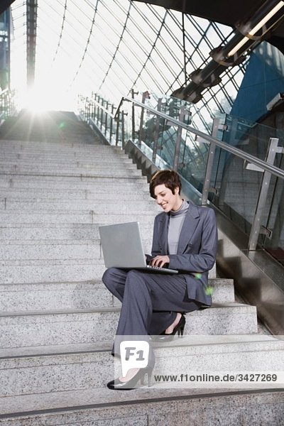 Geschäftsfrau in der U-Bahn-Station mit Laptop  auf der Treppe sitzend