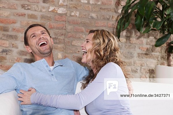 Germany  Cologne  Couple sitting on sofa  laughing  portrait