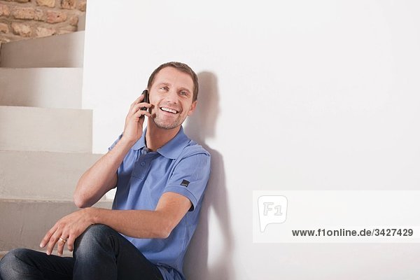 Mann auf Treppenstufen sitzend  mit Handy  lächelnd  Porträt