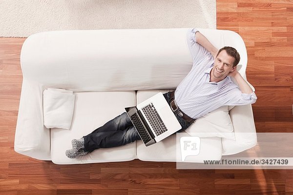 Mann mit Laptop entspannt auf Sofa  erhöhter Blick