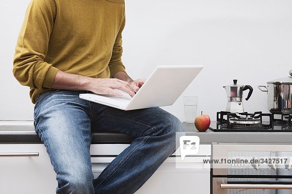 Man sitting on kitchen worktop  using laptop