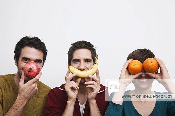 Männer und Frauen halten Früchte vor dem Gesicht.
