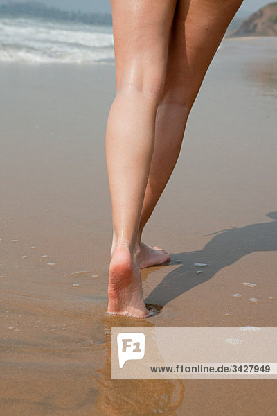 Beine einer Frau  die auf nassem Sand läuft.