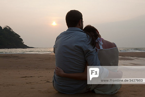 Paar bei Sonnenuntergang am Strand sitzen