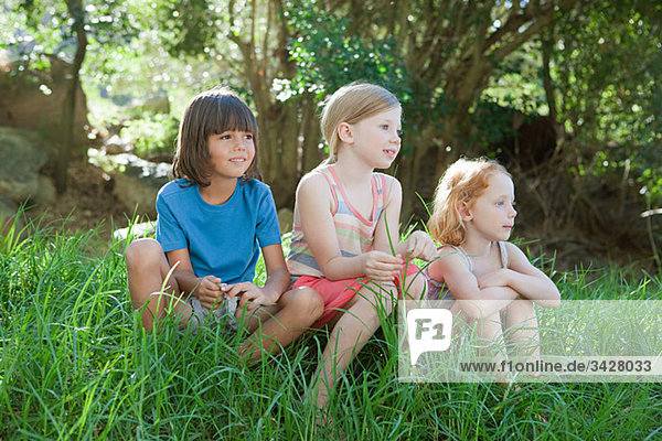 Drei Kinder sitzen auf Gras