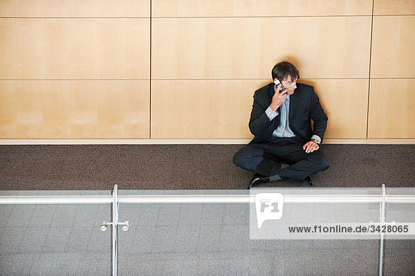 Businessman sitting in corridor using cellphone