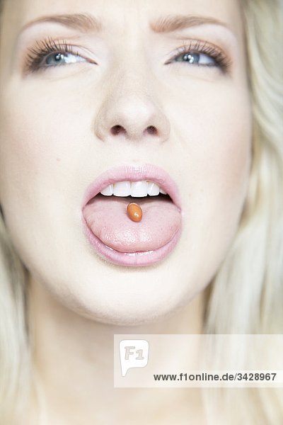 Young woman with a pill on her tongue  close-up