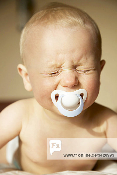 Baby weint mit Schnuller im Mund  Porträt