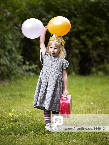 Scandinavia  Sweden  Stockholm  Girl wearing crown standing in park holding balloons and bag