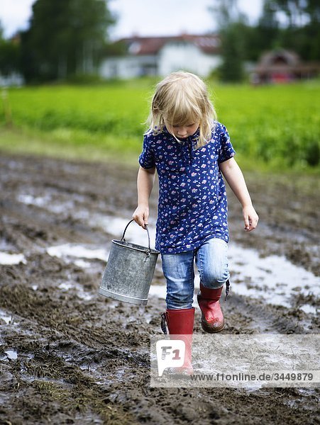 Scandinavia  Sweden  Girl (4-5) holding bucket walking through mud