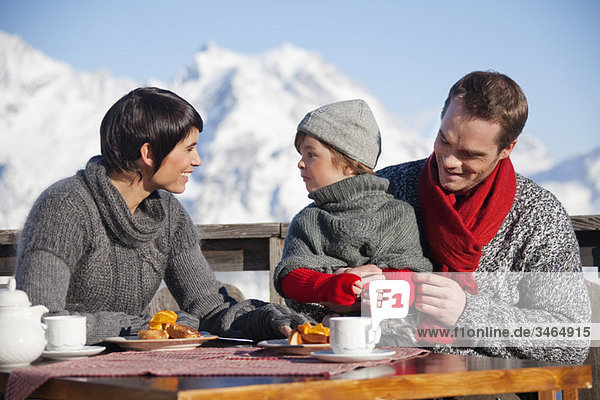 Paar und Tochter beim Essen auf dem Balkon im Skigebiet