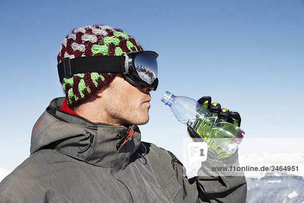 Junger Mann in Ski trägt Trinkwasser aus einer Flasche  Profil