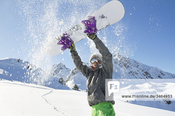 Junger Mann hält sein Snowboard über dem Kopf.